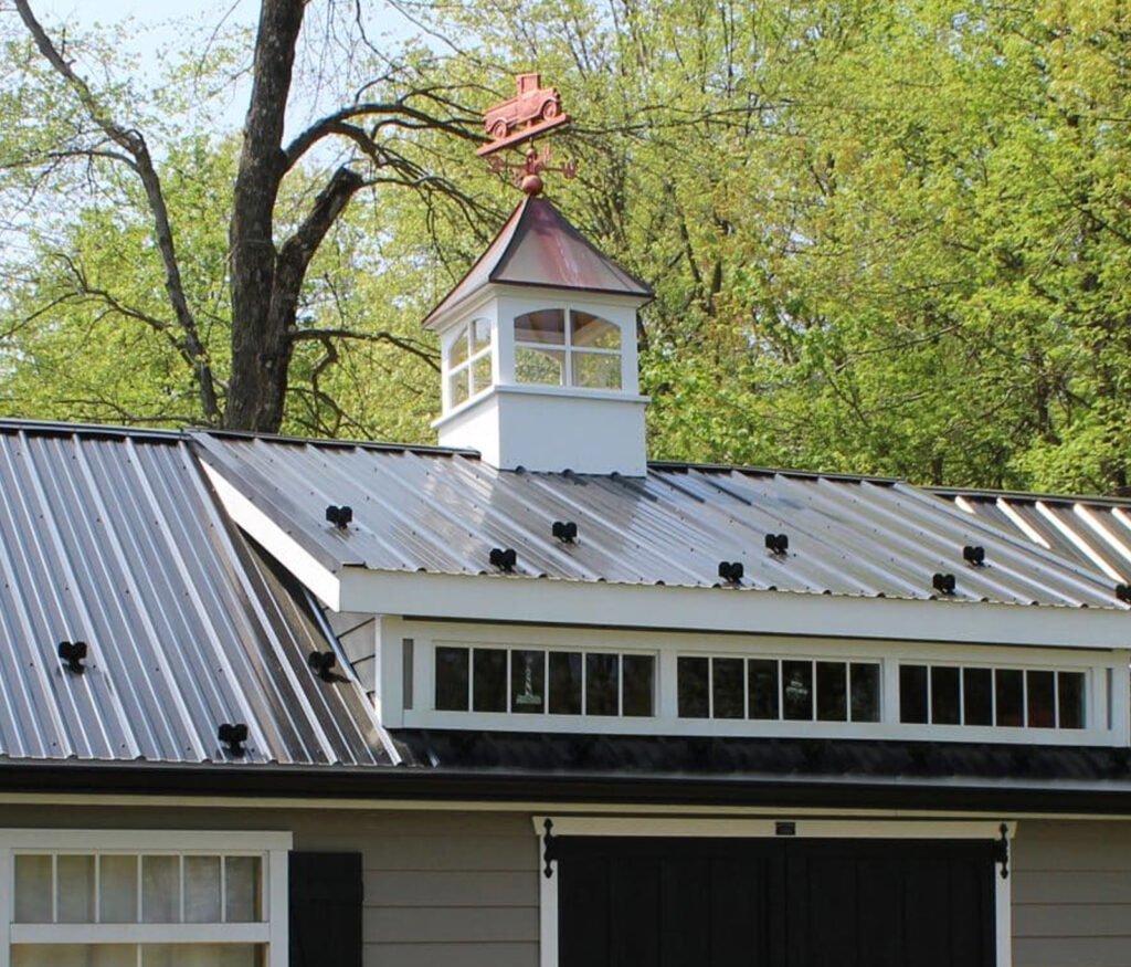 White vinyl cupola with windows and a copper roof featuring a vintage pickup truck weathervane on a brown metal roof.